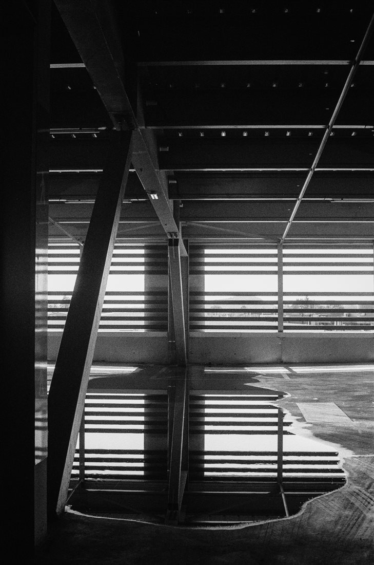 Ardèche, noir et blanc très graphique contrasté, vue intérieure détail parking couvert, poutres et garde-fous en métal reflétés dans une grande flaque d'eau